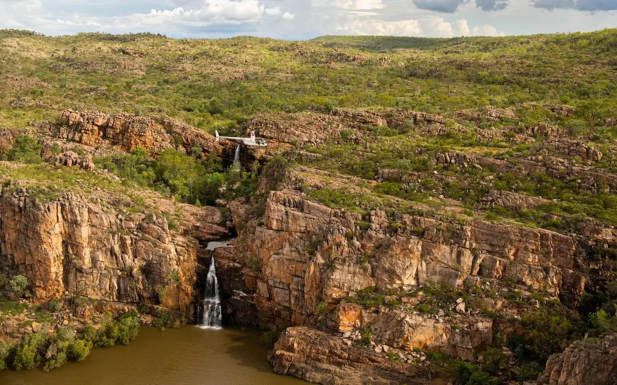 A waterfall dropping between red cliffs into a wide pool, seen from the air