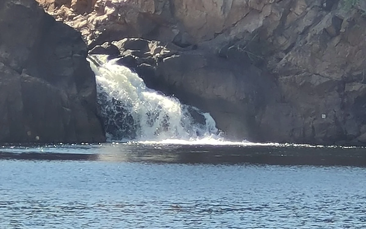 White water falling over a low rock ledge into a dark pool at Edith Falls