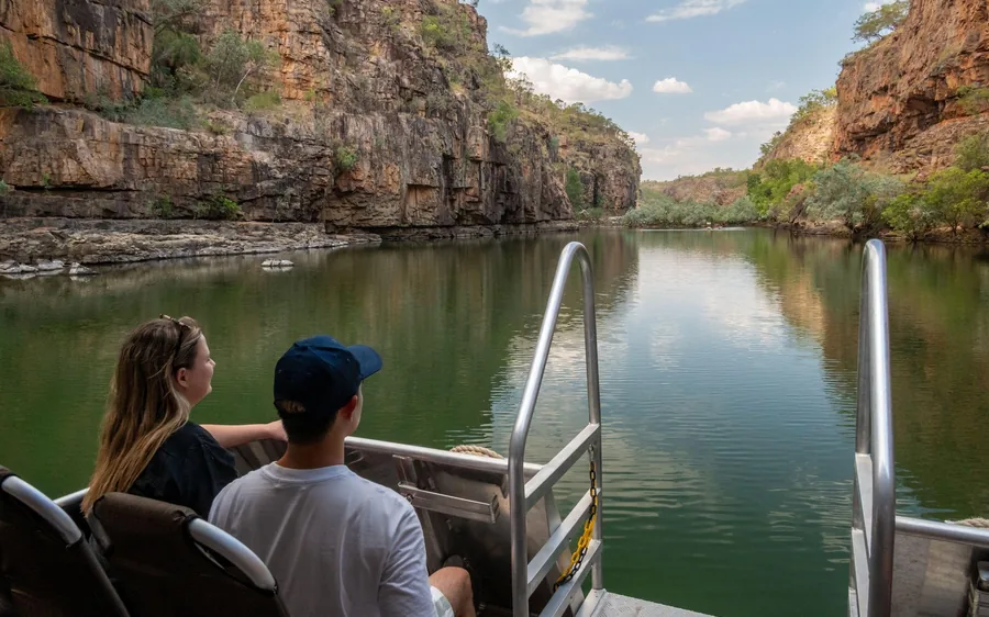 Two people on the open deck of a boat looking down a still, green-walled gorge