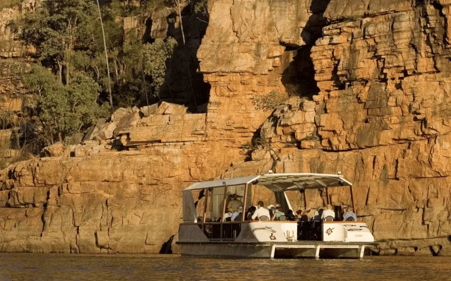 A flat-roofed tour boat moored below a tall golden sandstone wall