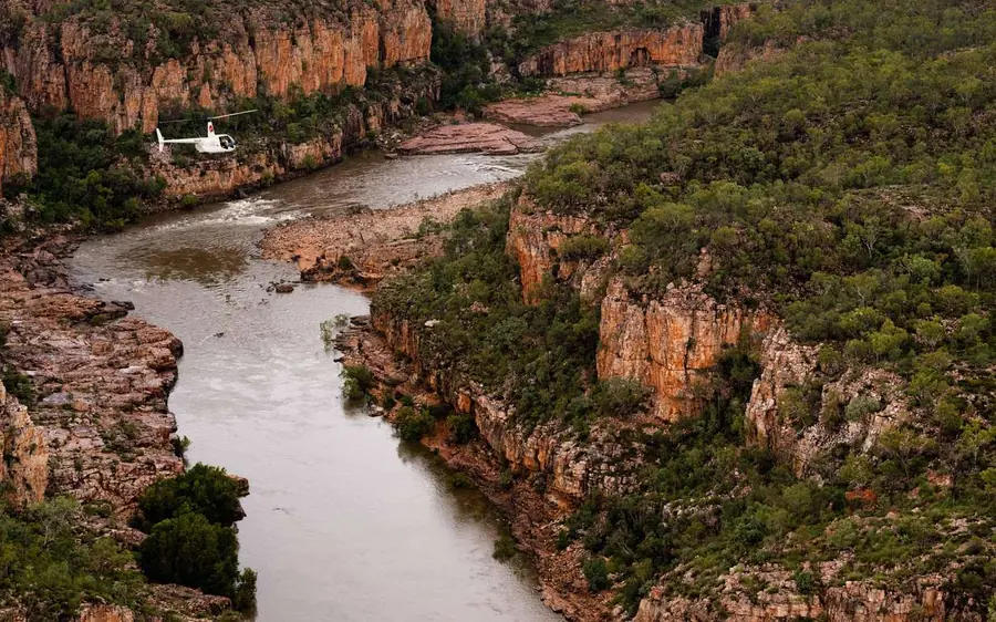 An aerial view of the brown river curving between low red cliffs and green scrub