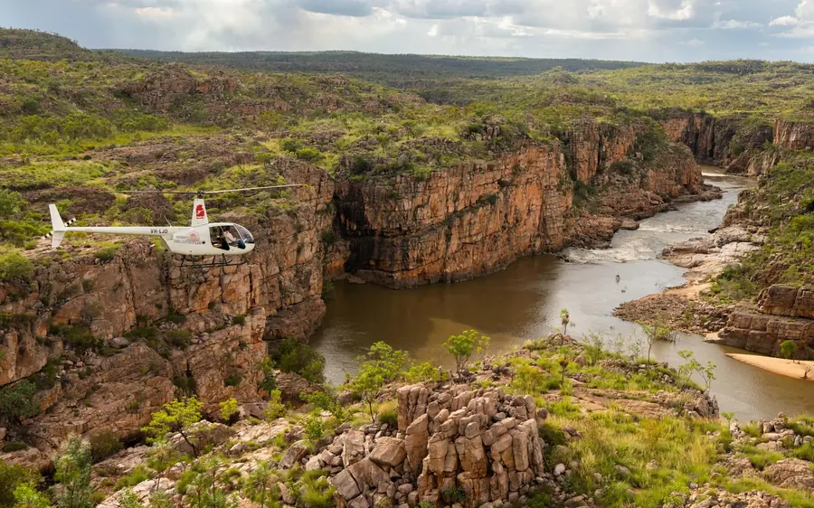 A small white helicopter parked on a clearing above the gorge, the river beyond