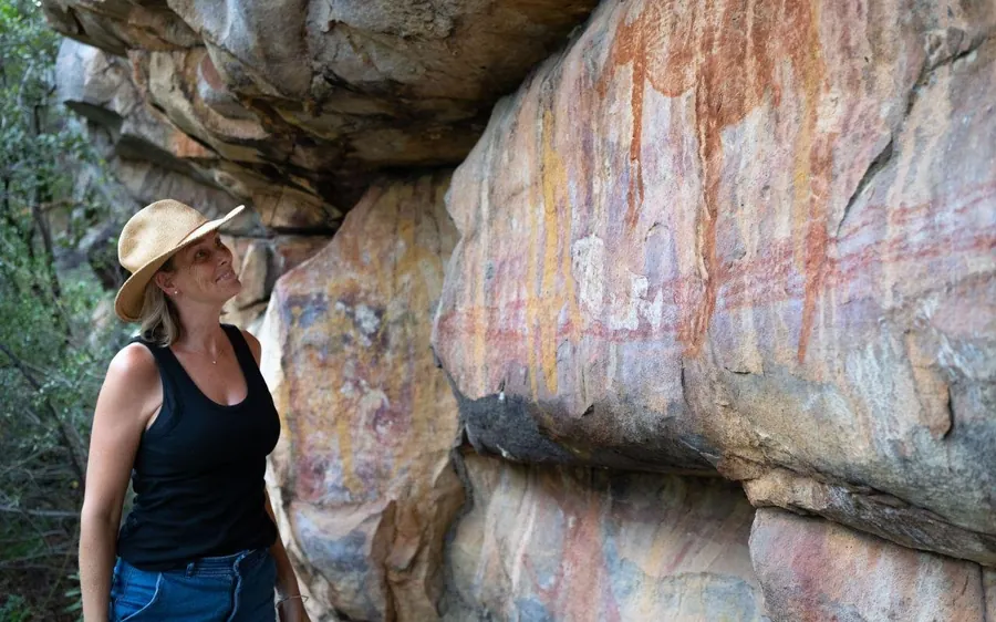 A woman in a wide hat looking up at a painted rock face under a stone overhang