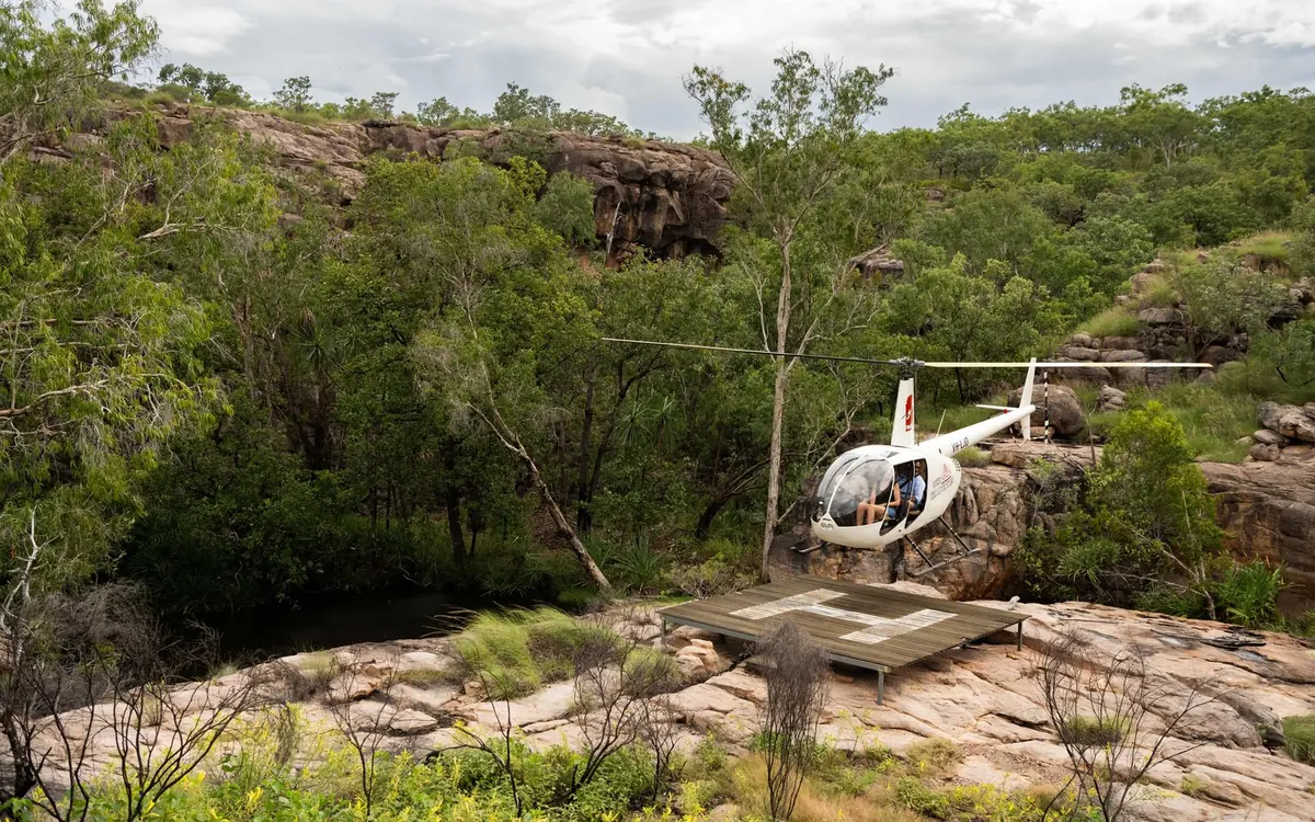 A helicopter beside a small timber landing deck on bare sandstone surrounded by bush